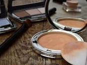 Close-up of makeup tools including compact, brush, and mirror on a rustic wooden surface.